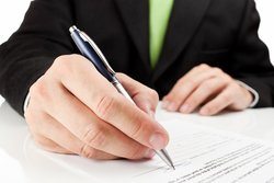 A man in a suit writing on a business document.