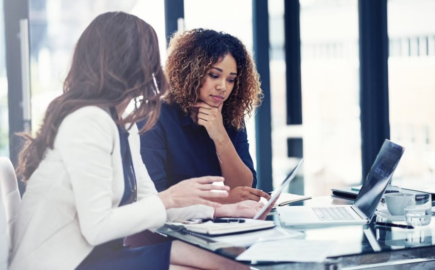 Two businesswomen using a digital tablet together during a collaboration at work.