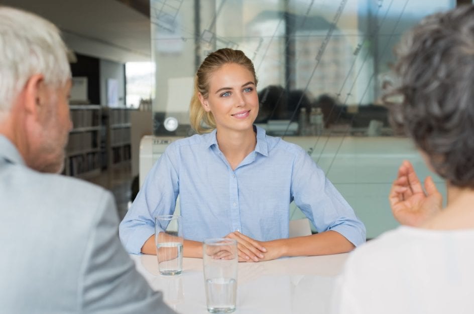 Portrait of beautiful young woman sitting in front of manager and senior leader during a job interview. Senior business people in conversation with a young business woman. Recruiter checking the candidate during job interview.